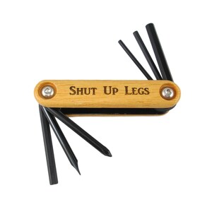 Peut inclure: Un outil multifonction en bois avec une poign&eacute;e noire et le texte "SHUT UP LEGS" grav&eacute; sur la poign&eacute;e. L'outil poss&egrave;de plusieurs cl&eacute;s Allen.