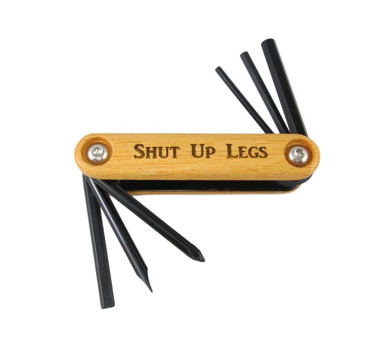 Peut inclure: Un outil multifonction en bois avec une poign&eacute;e noire et le texte "SHUT UP LEGS" grav&eacute; sur la poign&eacute;e. L'outil poss&egrave;de plusieurs cl&eacute;s Allen.