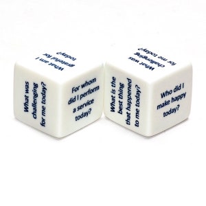 May include: Two white dice with blue text. The dice are used for a reflection game. The text on the dice includes questions like "What was challenging for me today?" and "What is the best thing that happened to me today?"