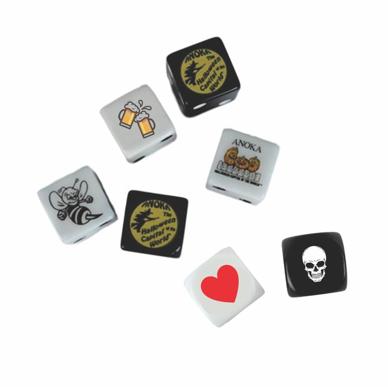 May include: A set of six black and white dice with various images, including a bee, a beer mug, a heart, a skull, and pumpkins. The dice are printed with the text "Anoka, The Halloween Capital of the World".