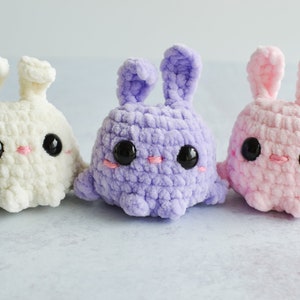 Purple, cream, and pink chenille yarn crocheted bunnies with tall ears standing together in a row.