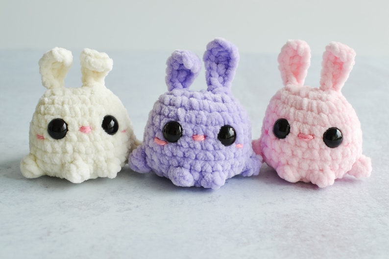 Purple, cream, and pink chenille yarn crocheted bunnies with tall ears standing together in a row.