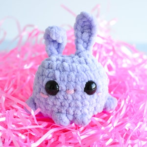 Purple chenille yarn crocheted bunny with tall ears standing in a pile of pink easter grass.