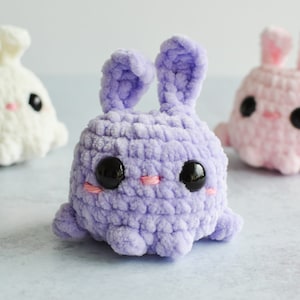 Purple, cream, and pink chenille yarn crocheted bunnies with tall ears staggered together.
