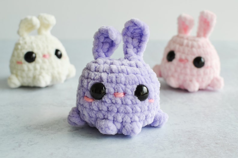 Purple, cream, and pink chenille yarn crocheted bunnies with tall ears staggered together.