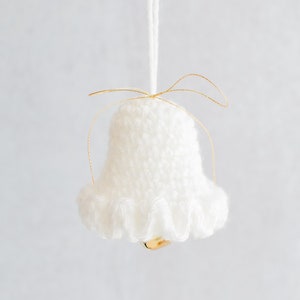 Op de afbeelding: Witte gebreide bel ornament met een gouden lint en een gouden bel erin.