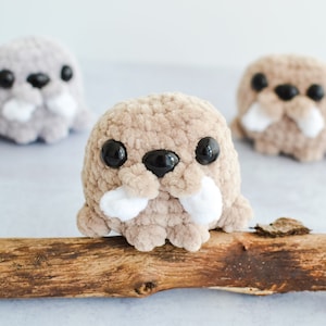May include: Three crocheted plush walrus toys. Two are grey and one is brown. The brown walrus is sitting on a branch.