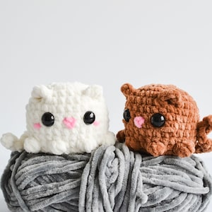 Può includere: Due animali di peluche all'uncinetto, uno bianco e uno marrone, seduti su un gomitolo di lana grigio. L'animale bianco ha occhi neri e guance rosa. L'animale marrone ha occhi neri e un naso rosa.