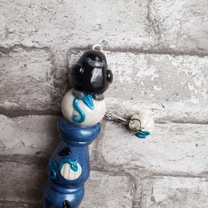 May include: A blue and white ceramic knitting needle with a black bird perched on top. The bird is sitting on a white sphere with a blue swirl design. The needle has a white sphere with a blue swirl design at the bottom.