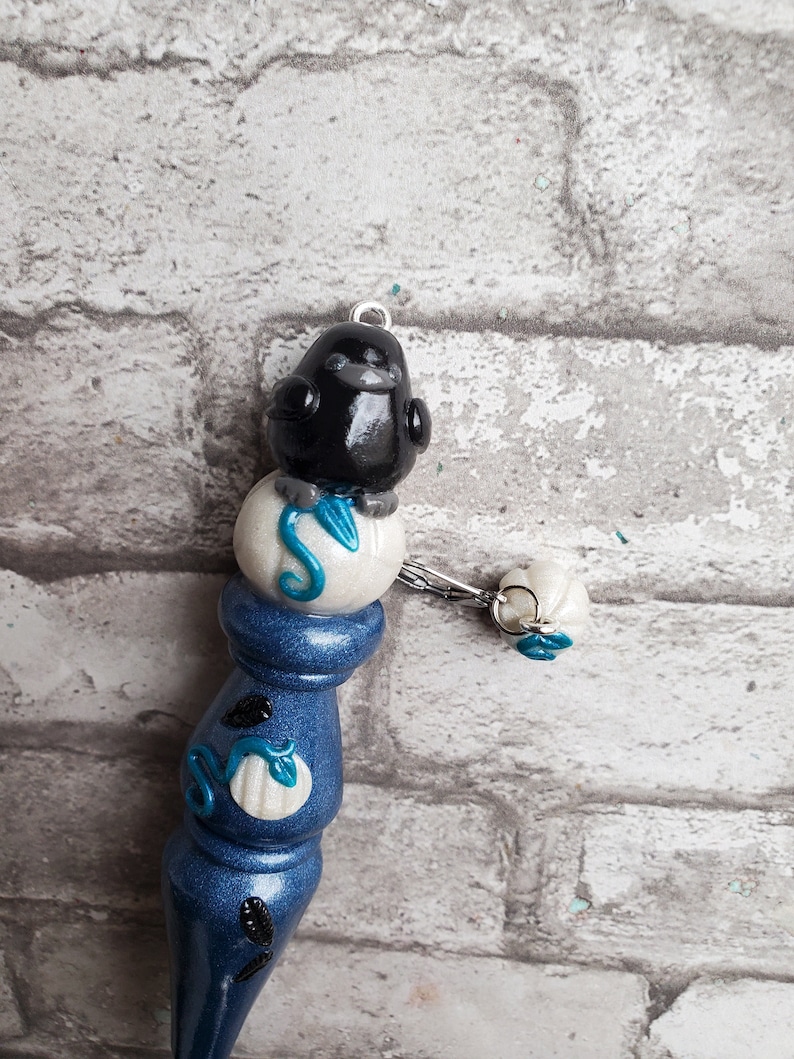 May include: A blue and white ceramic knitting needle with a black bird perched on top. The bird is sitting on a white sphere with a blue swirl design. The needle has a white sphere with a blue swirl design at the bottom.