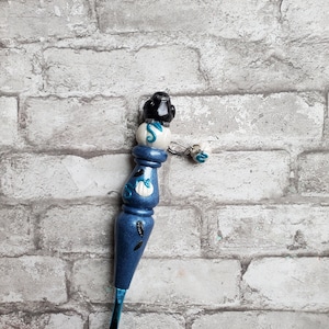 May include: A blue crochet hook with a white and black handle. The handle is decorated with a seashell and a starfish. The hook has a blue and white tassel.