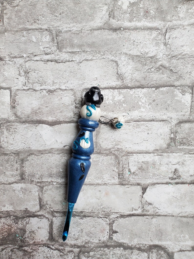 May include: A blue crochet hook with a white and black handle. The handle is decorated with a seashell and a starfish. The hook has a blue and white tassel.