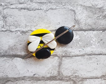 May include: A yellow and black bee-shaped needle minder with a white wing design. The needle minder is attached to a black magnetic disc.