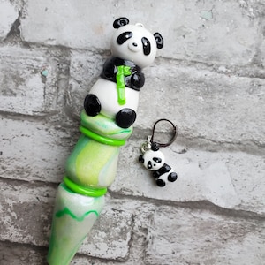 May include: A green and white crochet hook with a panda bear charm. The panda is holding a piece of green bamboo. The hook is decorated with green and white swirls.