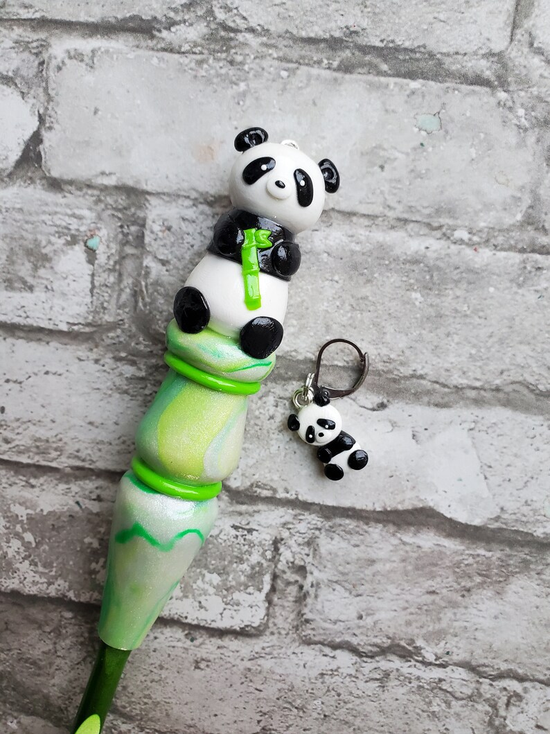May include: A green and white crochet hook with a panda bear charm. The panda is holding a piece of green bamboo. The hook is decorated with green and white swirls.