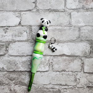 May include: Green and white crochet hook with a panda bear charm. The hook is made of wood and has a green and white swirl pattern. The panda bear charm is attached to the hook with a silver ring.