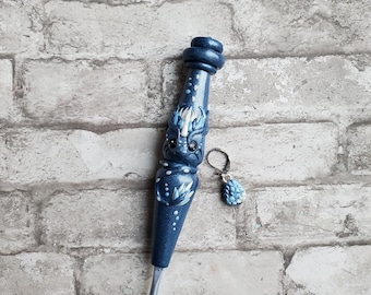 Pode incluir: Um gancho de crochê azul com um design de dragão branco e um brinco azul e branco.