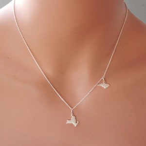 May include: A silver necklace with two charms, one shaped like the state of New York and the other shaped like the state of North Carolina.