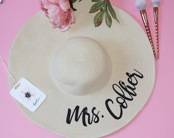 May include: A beige straw sun hat with a black inscription that reads "Mrs. Collier".