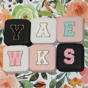 Peut inclure: Six petites boîtes carrées avec des couvercles de couleurs différentes. Chaque boîte a une grande lettre sur le couvercle, épellant "YAWKS". Les lettres sont blanches, noires, roses et bleues avec des bordures dorées.