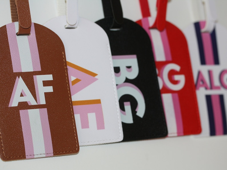 May include: A collection of five rectangular luggage tags in brown, white, black, red, and white, each featuring a vertical stripe pattern and bold, capitalized monogram letters including AF, AE, BG, SG, and ALG in various color combinations.
