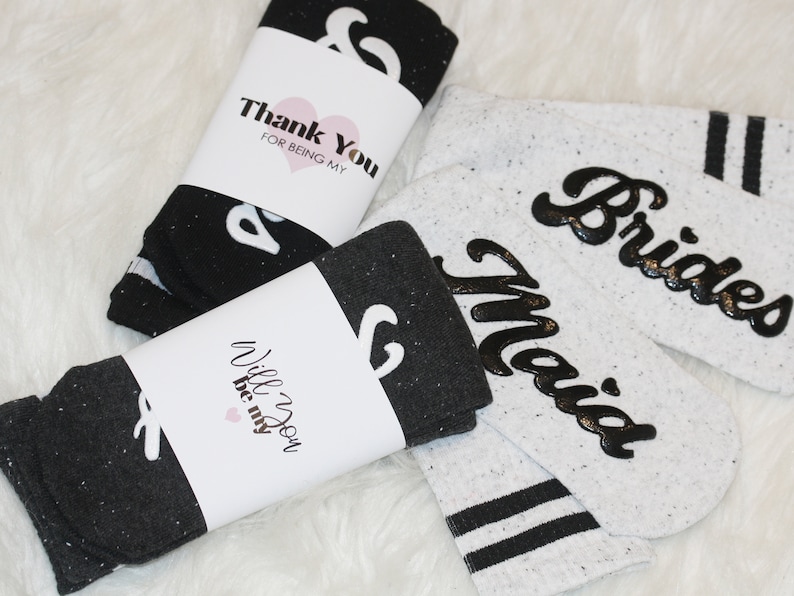 K&ouml;nnte beinhalten: Zwei Paar Socken mit einem schwarz-wei&szlig;en, gesprenkelten Muster. Ein Paar hat den Text "Will you be my" und das andere Paar hat den Text "Brides Maid".