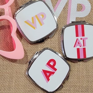 May include: Three silver compact mirrors with white backgrounds and colorful lettering. The mirrors have the letters "VIP", "AT", and "AP" on them.