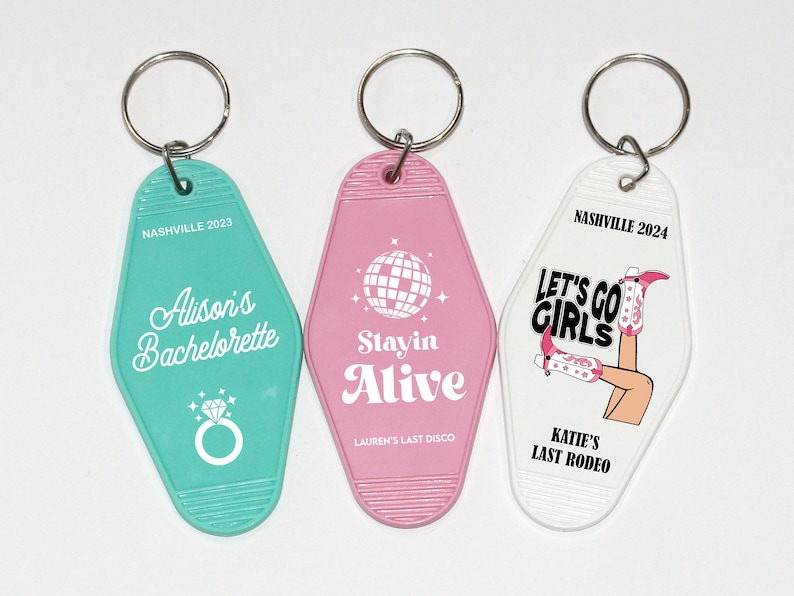 May include: Three keychains with different designs. The first keychain is turquoise blue with the text "Nashville 2023 Alison's Bachelorette" and a diamond ring. The second keychain is pink with the text "Stayin Alive Lauren's Last Disco" and a disco ball. The third keychain is white with the text "Nashville 2024 Let's Go Girls Katie's Last Rodeo" and a woman wearing cowboy boots.