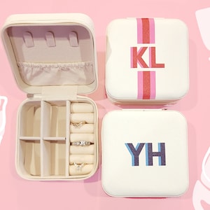 May include: Three white square jewelry boxes with different colored stripes and personalized initials. The box on the left is open and shows a compartment for rings and earrings.