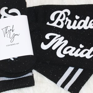 K&ouml;nnte beinhalten: Schwarze Socken mit wei&szlig;en Streifen und den Worten "Brides Maid" und "Thank You for being my..." darauf gedruckt.