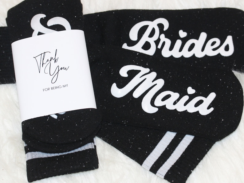 K&ouml;nnte beinhalten: Schwarze Socken mit wei&szlig;en Streifen und den Worten "Brides Maid" und "Thank You for being my..." darauf gedruckt.