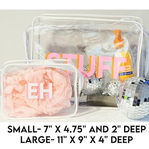 May include: Two clear plastic zippered bags with white trim. The smaller bag is 7 inches by 4.75 inches and 2 inches deep. The larger bag is 11 inches by 9 inches and 4 inches deep. The smaller bag has the letters "EH" in pink and orange on the front. The larger bag has the word "STUFF" in pink and orange on the front.
