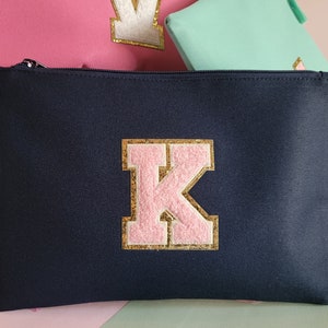 May include: A navy blue zippered pouch with a pink and gold letter K on the front.