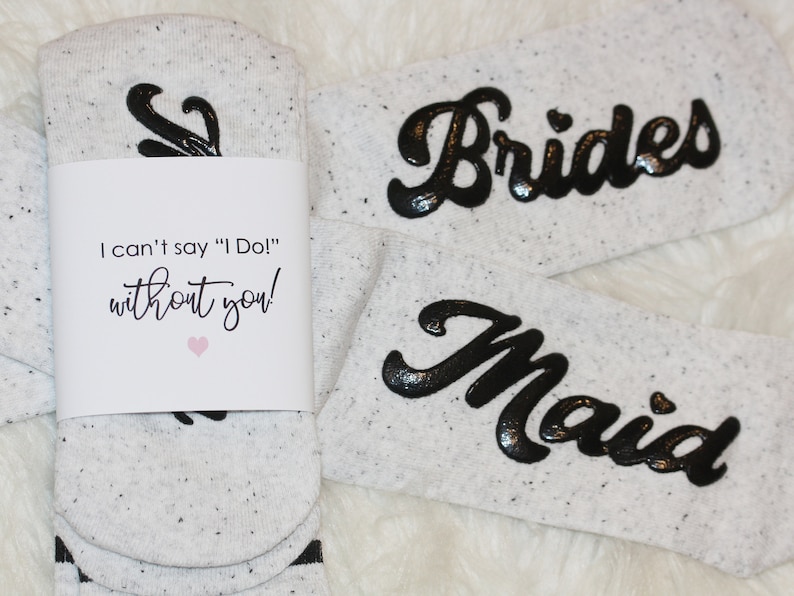 K&ouml;nnte beinhalten: Zwei Paar wei&szlig;e Socken mit schwarzer Beschriftung. Ein Paar sagt "Brides" und das andere sagt "Maid". Ein wei&szlig;es Etikett ist an einem Paar Socken befestigt, auf dem steht "Ich kann nicht "Ich tue es!" sagen, ohne dich!"