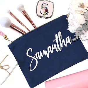 May include: A navy blue canvas makeup bag with a white zipper and the name "Samantha" printed in white cursive lettering.