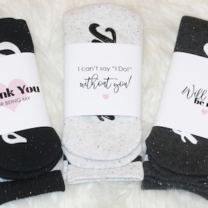K&ouml;nnte beinhalten: Drei Paar Socken mit wei&szlig;en und schwarzen Ampersand-Designs. Jedes Paar ist in ein wei&szlig;es Papierband mit einer anderen Botschaft verpackt: "Danke, dass du mein bist", "Ich kann nicht "Ich tue es!" sagen, ohne dich!" und "Willst du mein sein".