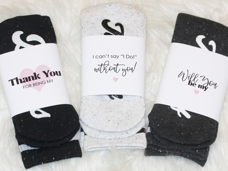 K&ouml;nnte beinhalten: Drei Paar Socken mit wei&szlig;en und schwarzen Ampersand-Designs. Jedes Paar ist in ein wei&szlig;es Papierband mit einer anderen Botschaft verpackt: "Danke, dass du mein bist", "Ich kann nicht "Ich tue es!" sagen, ohne dich!" und "Willst du mein sein".
