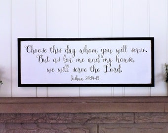 May include: A white wooden sign with black lettering and a black frame. The sign reads "Choose this day whom you will serve. But as for me and my house, we will serve the Lord. Joshua 24:14-15".