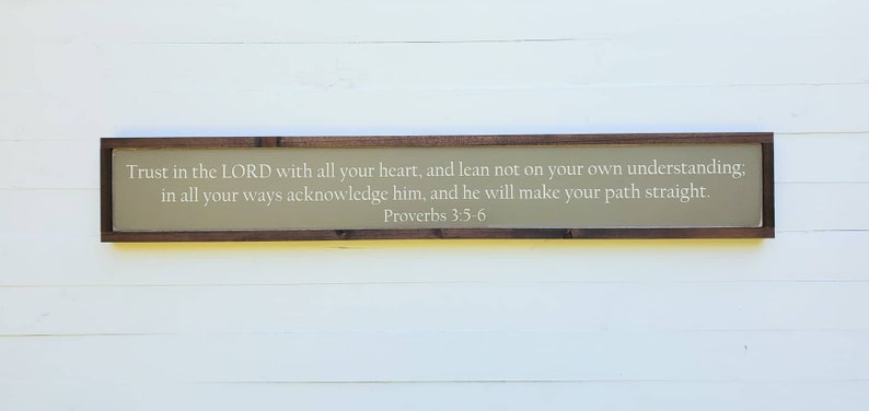 May include: A wooden sign with a beige background and a brown frame. The sign features a white inscription with the text "Trust in the LORD with all your heart, and lean not on your own understanding; in all your ways acknowledge him, and he will make your path straight. Proverbs 3:5-6".