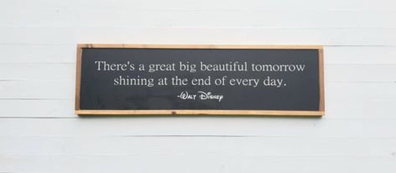 Puede incluir: Un letrero de pared rectangular con fondo negro y marco de madera natural. El texto en blanco dice: There's a great big beautiful tomorrow shining at the end of every day. -Walt Disney. El letrero est&aacute; orientado horizontalmente.