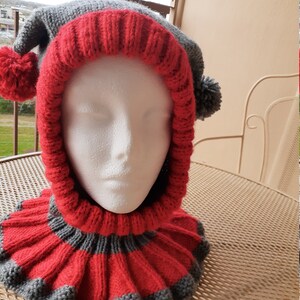 Puede incluir: Un gorro de punto gris y rojo con un pomp&oacute;n a cada lado. El gorro tiene un cuello largo de punto a juego, tambi&eacute;n a rayas en gris y rojo.