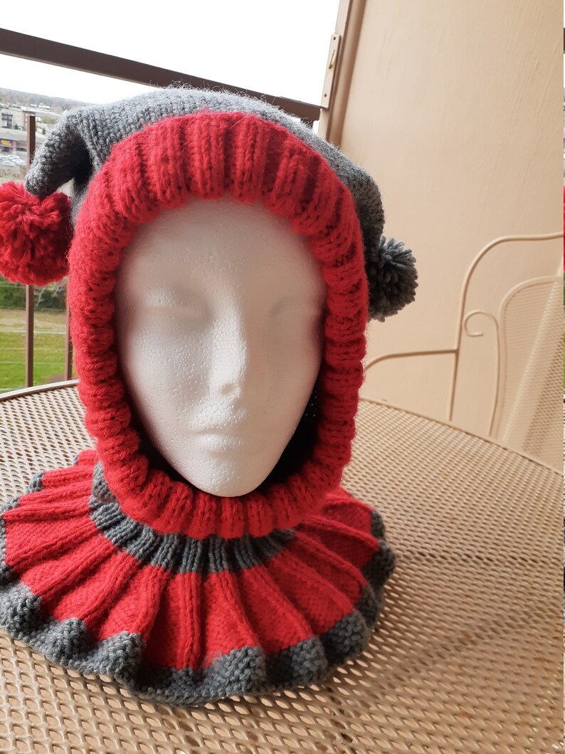 Puede incluir: Un gorro de punto gris y rojo con un pomp&oacute;n a cada lado. El gorro tiene un cuello largo de punto a juego, tambi&eacute;n a rayas en gris y rojo.