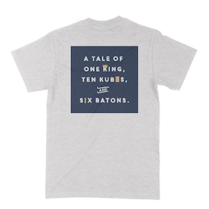 May include: A gray t-shirt with a navy blue square on the back. The square has the text "A Tale of One King, Ten Kubis, and Six Batons." in white.