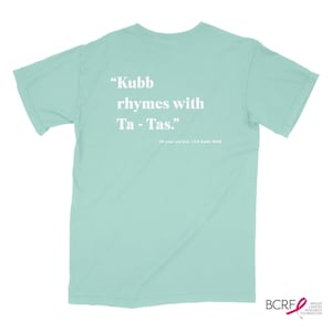 May include: A light blue t-shirt with white text that reads "Kubb rhymes with Ta - Tas."  The text is attributed to a 10 year old kid, USA Kabb 2018.