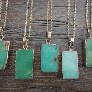 May include: Five gold necklaces with green gemstone pendants. Each pendant is a rectangular shape with a gold trim.