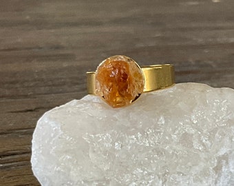 May include: A gold ring with a large, orange, natural citrine gemstone set in a bezel setting.