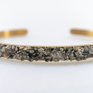 May include: A gold bangle bracelet with a band of small, dark gray pyrite stones.