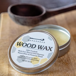 May include: A silver tin of wood wax with a white label that reads "WARLYWOOD WOOD WAX 100% Foodsafe Made from Mineral Oil & Beeswax Repels Water & Preserves Wood Apply as often as you desire to keep your wood looking its best. NET WT. 8.0 OZ"
