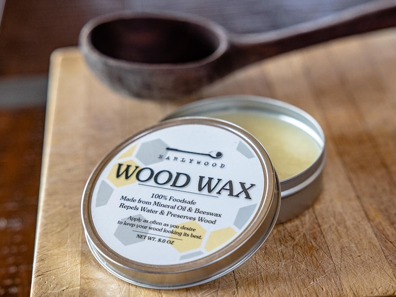 May include: A silver tin of wood wax with a white label that reads "WARLYWOOD WOOD WAX 100% Foodsafe Made from Mineral Oil & Beeswax Repels Water & Preserves Wood Apply as often as you desire to keep your wood looking its best. NET WT. 8.0 OZ"