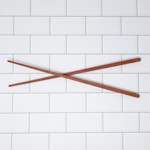 May include: Two wooden chopsticks crossed over each other against a white tiled background.